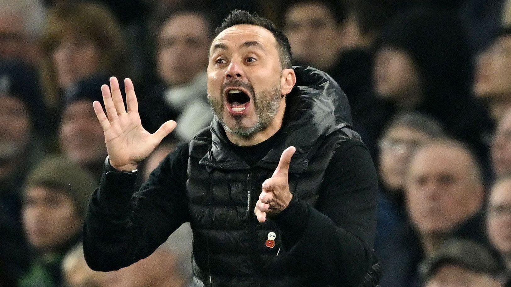 Tottenham Hotspur head coach Roberto de Zerbi looks animated with his mouth wide open and both hands out in front of him as if about to applaud, as he wears a black padded jacket, which has a poppy badge attached