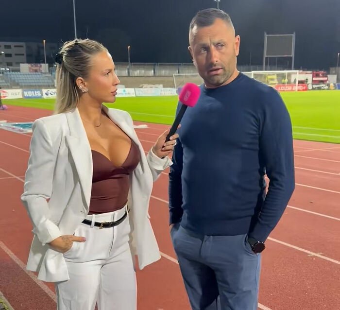 Coach looking away awkwardly while female reporter interviews him on football field