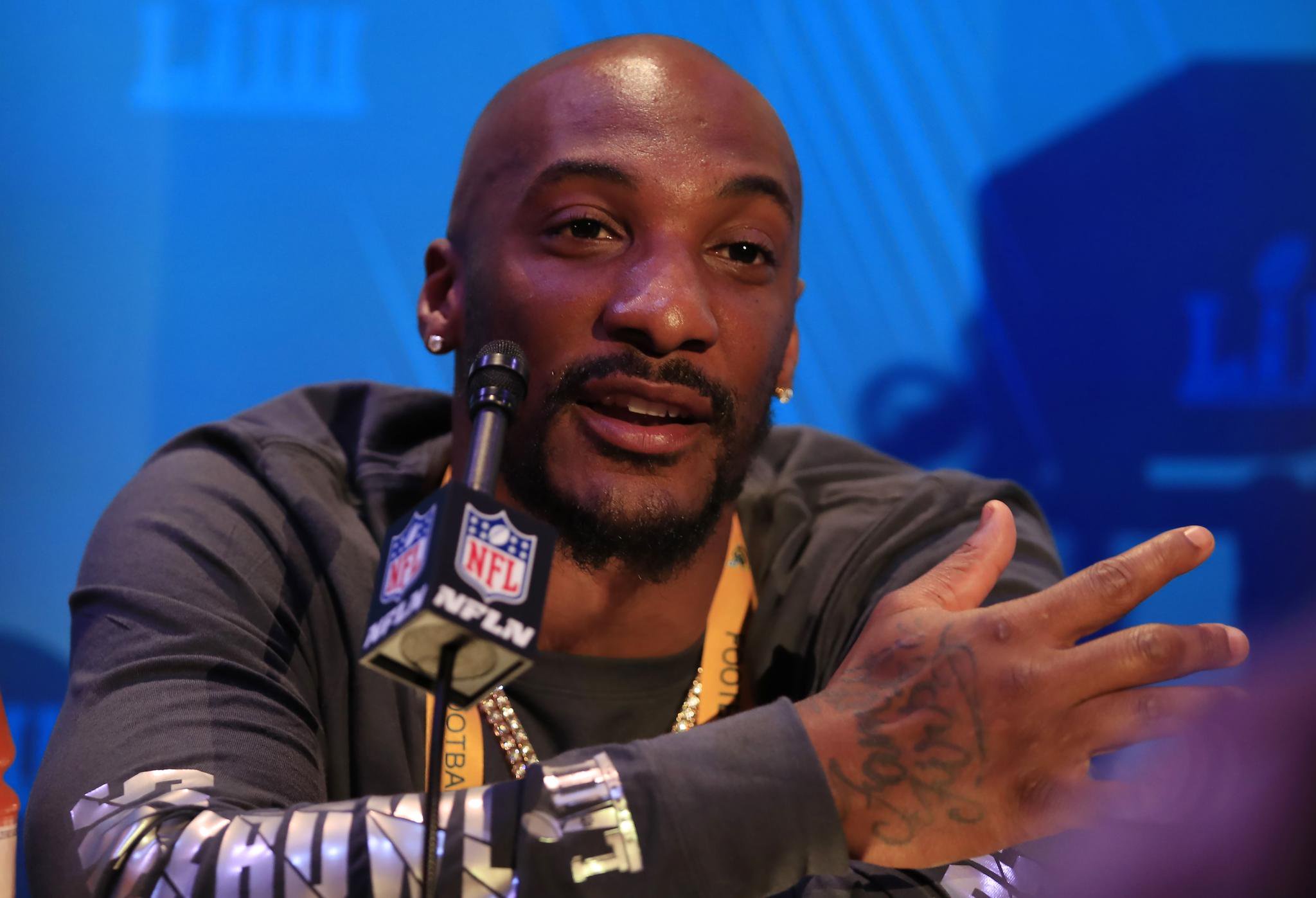 A bald man speaking at a microphone during the Super Bowl LIII Opening Night.