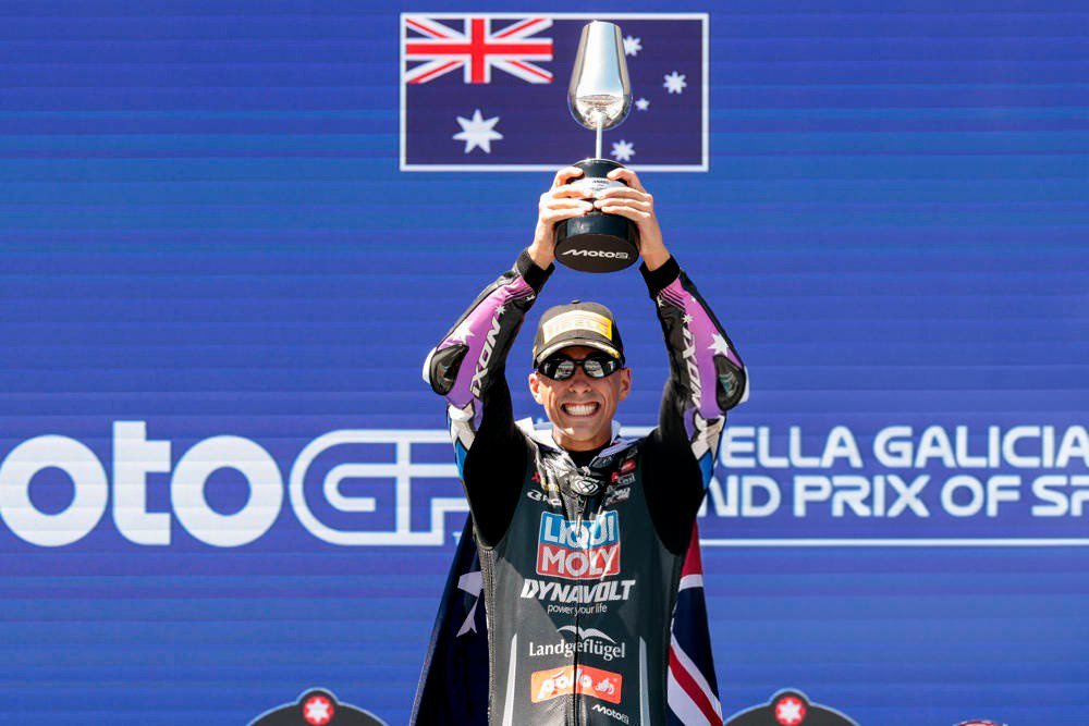 Senna Agius celebrates on the podium holding a trophy aloft at the Galician Grand Prix of Spain, wearing a Liqui Moly Dynavolt team suit.