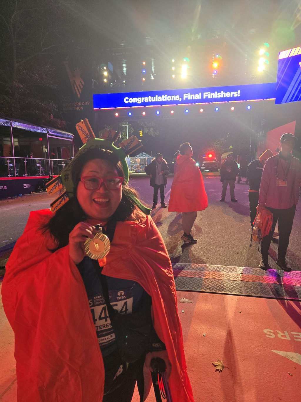 Teresa Hui smiles and holds up her medal while wrapped in a poncho at the New York City Marathon finish line.