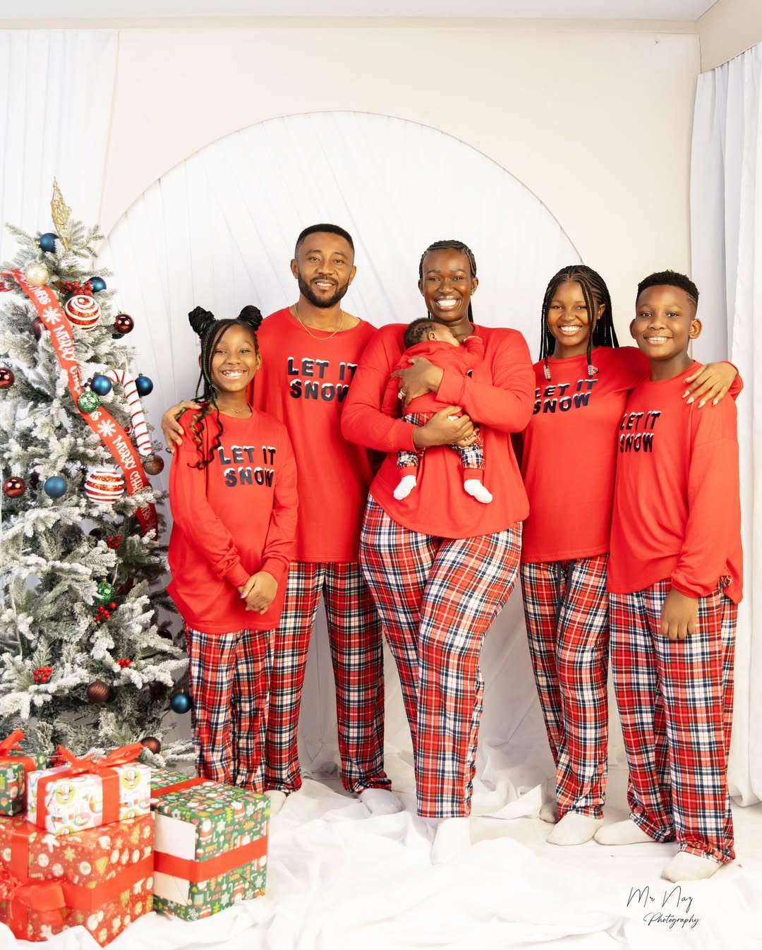 Comedian Warri Pikin poses with her family in matching red Christmas outfits beside a decorated Christmas tree