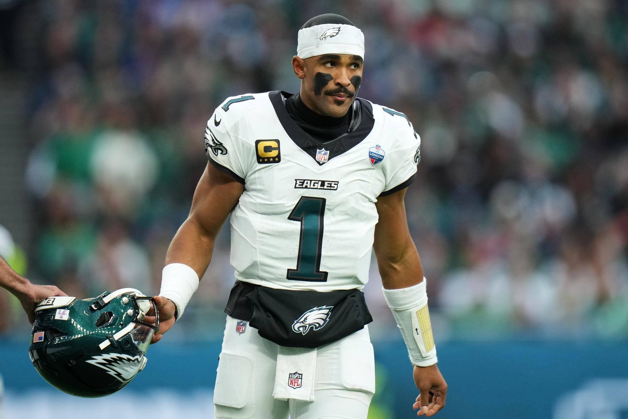 Philadelphia Eagles quarterback Jalen Hurts stands on the field holding his helmet.