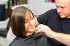 Haircut of short hair of young woman by a male hairdresser.
