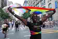 A person on the parade route wearing a rainbow colored shirt and holding a pride flag over their head.