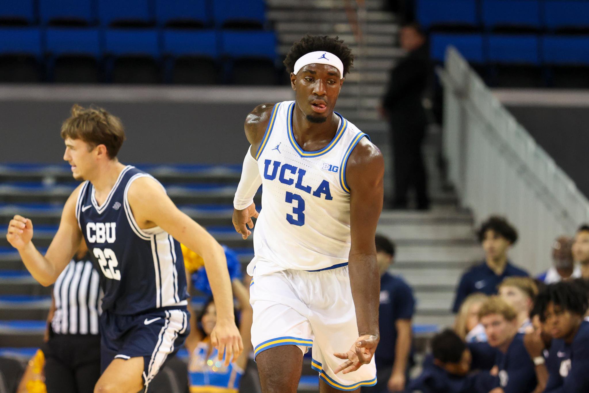 A basketball player in a white UCLA uniform with the number 3 on the front runs down the court during a game against Cal Baptist.