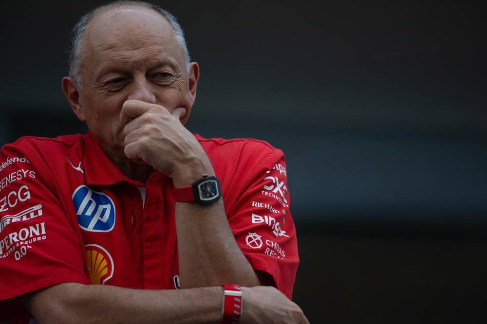 A man in a red Scuderia Ferrari team shirt with HP, Shell and Pirelli logos, hand to his chin, in the F1 paddock at Austin