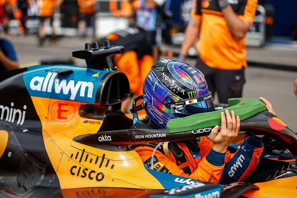 Oscar Piastri in his McLaren MCL40 F1 car in the pit lane, wearing a helmet with Monster branding and a McLaren orange race suit.