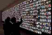 FILE - Visitors look at photos of Israeli people who were killed during the Hamas attack on Oct. 7 and those who died during the Israel-Hamas war in the Gaza Strip, displayed on a giant screen at the National Library in Jerusalem, Israel, Jan. 28, 2024. (AP Photo/Leo Correa, File)