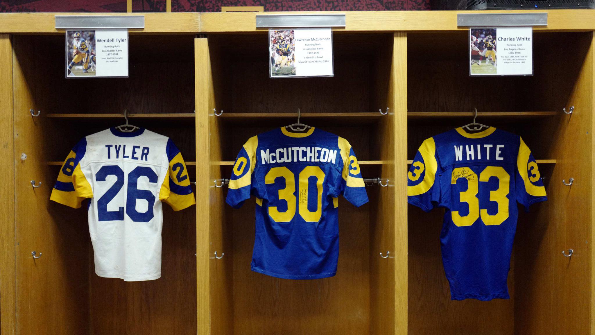 Three Los Angeles Rams jerseys for Wendell Tyler, Lawrence McCutcheon, and Charles White hanging in lockers.