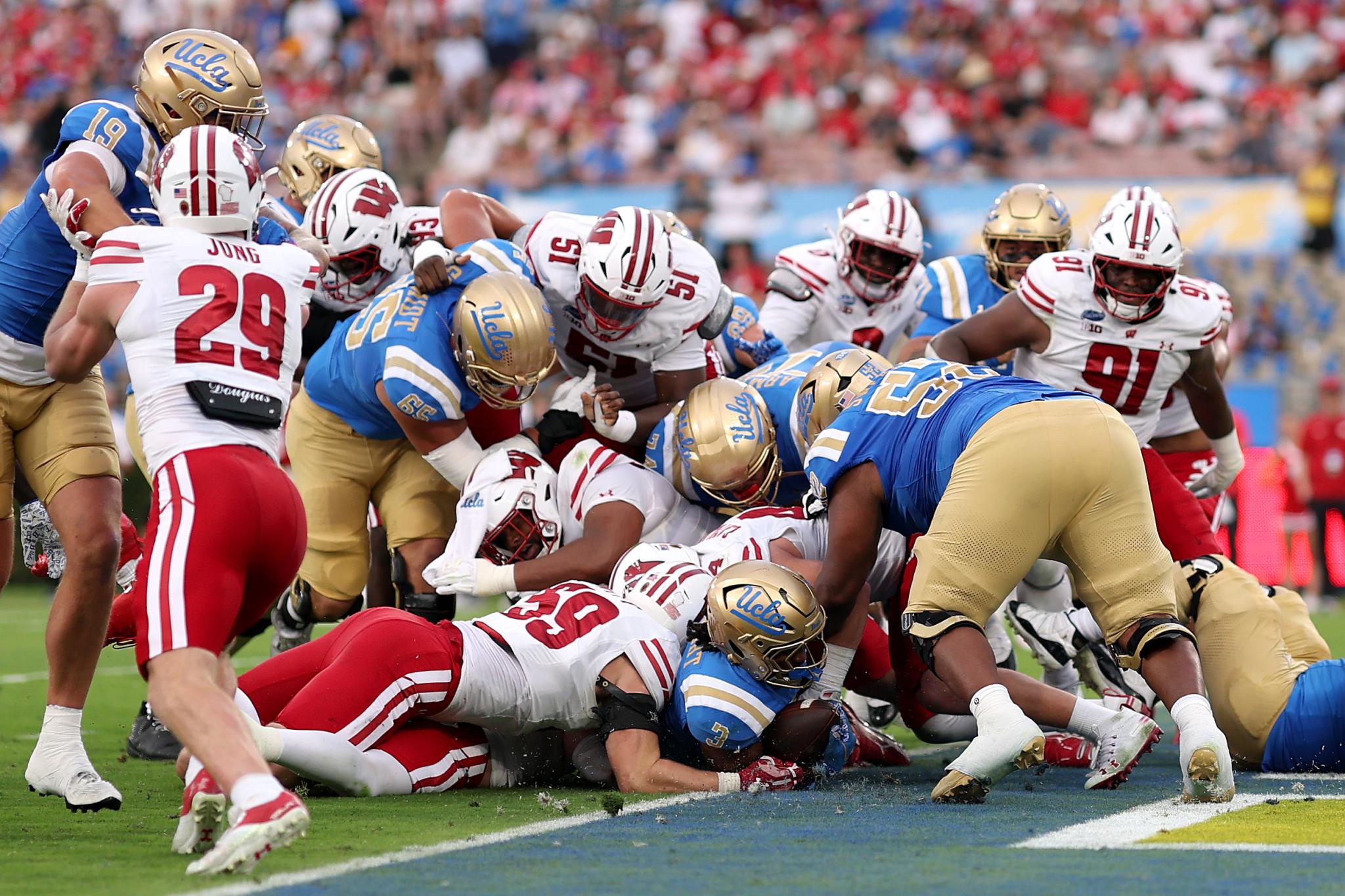 Football players from Wisconsin and UCLA are tangled in a pileup on the field.
