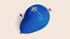 A photo illustration shows a balloon with the NATO logo about to be deflated by sticks with the flags of the USA and France.