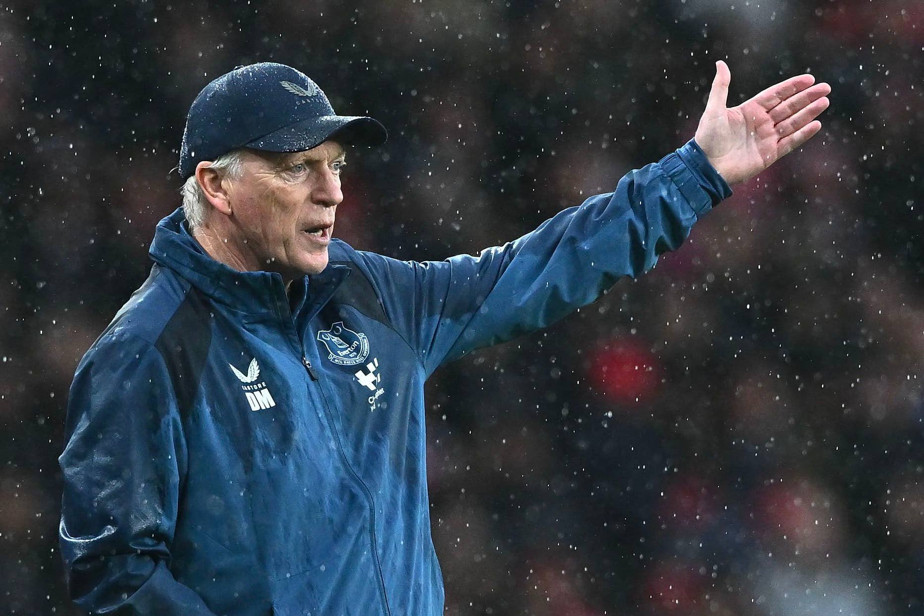 Everton-Trainer David Moyes steht in einer blauen Regenjacke und Baseballcap am Spielfeldrand und gestikuliert mit ausgestrecktem Arm.