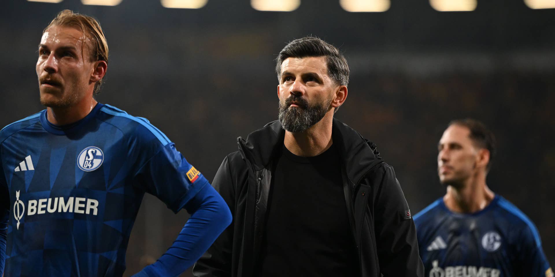 Drei enttäuschte Schalke-Spieler und ihr Trainer nach einer Niederlage im Fußballstadion.