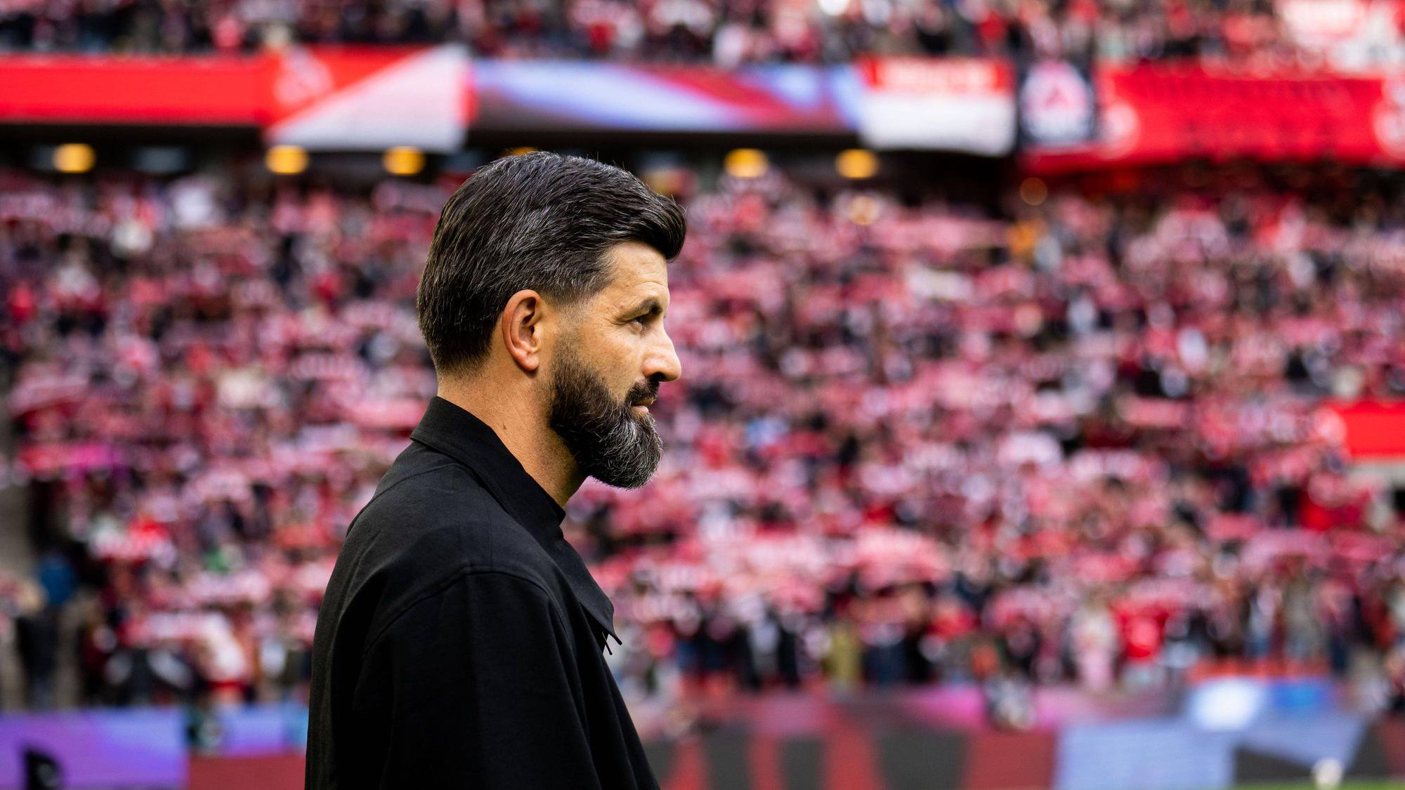 Miron Muslic steht im Stadion, im Hintergrund sind FC-Fans zu sehen.