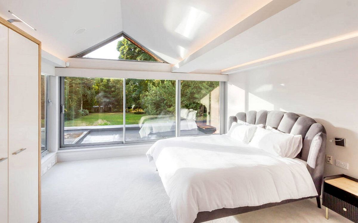 An interior view of a luxurious bedroom featuring a large bed with white bedding, a glass window that opens to a scenic outdoor view, and minimalist decor with a modern aesthetic.