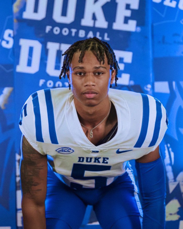 Star football player in Duke uniform posing for portrait in front of Duke football backdrop