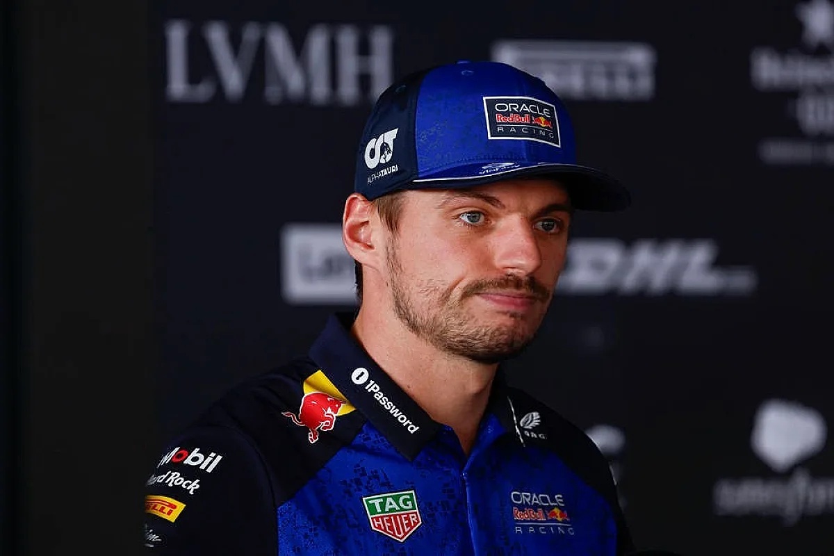 A Red Bull Racing driver in a blue team shirt and cap speaks at a press event, with LVMH and DHL sponsor branding behind him, F1 paddock