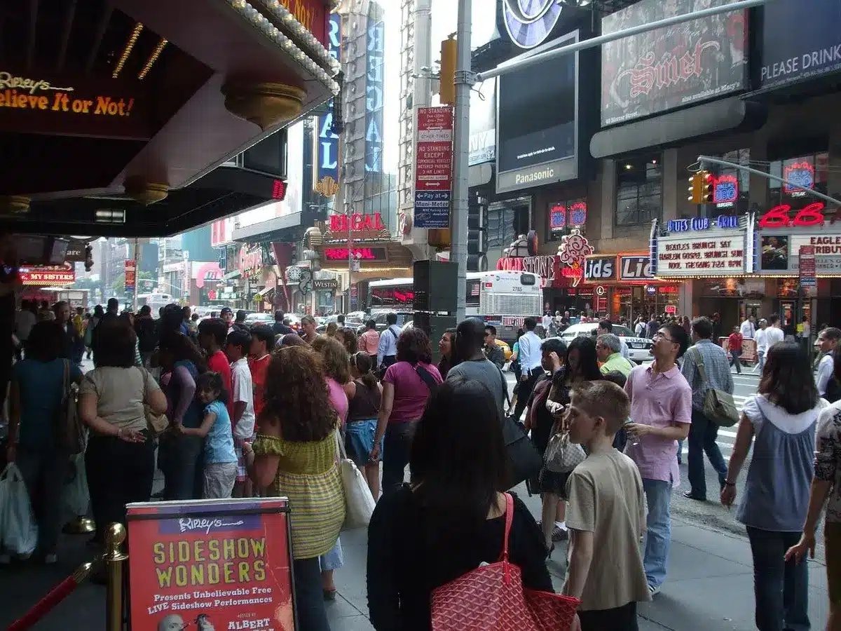 Crowd-lined street outside a theatre with phones held over barriers, evening atmosphere, police barriers visible