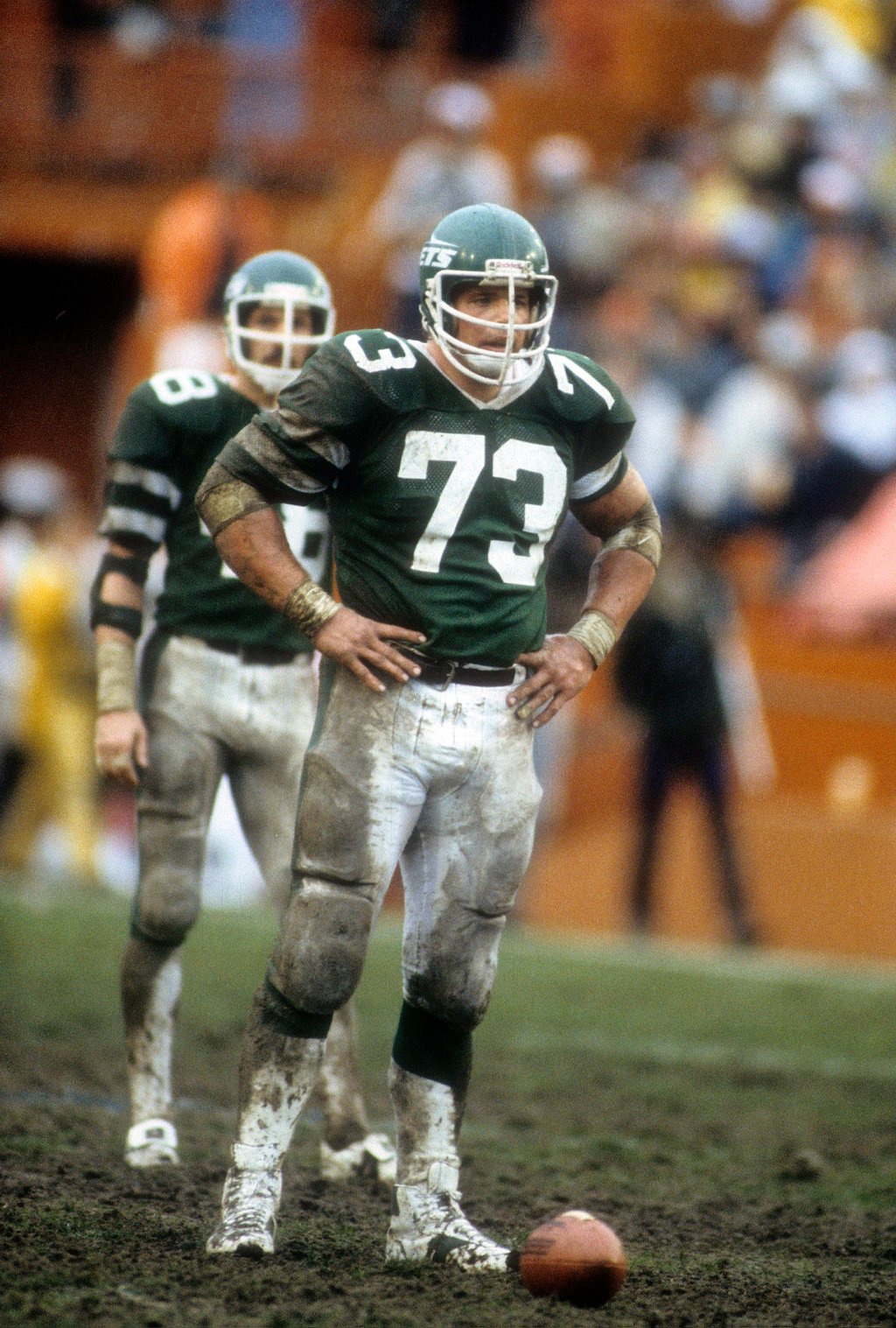 Two New York Jets players stand on a muddy field during a game against the Miami Dolphins.