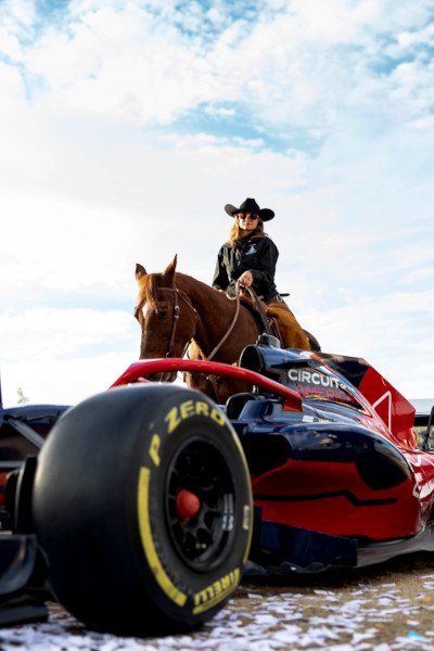 A cowgirl on a horse next to a racecar