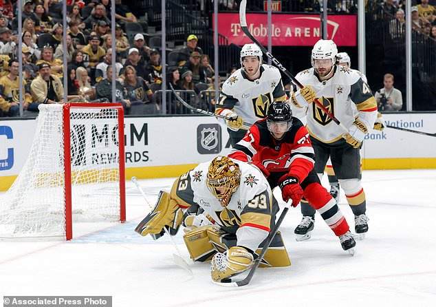 Vegas Golden Knights goaltender Adin Hill (33) covers the puck in front pf New Jersey Devils right wing Luke Evangelista (77) during the second period of an NHL hockey game Friday, Oct. 30, 2026, in Las Vegas. (Steve Marcus/Las Vegas Sun via AP)