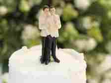 A wedding cake topper featuring two figurines of men in suits, standing closely together with their arms around each other