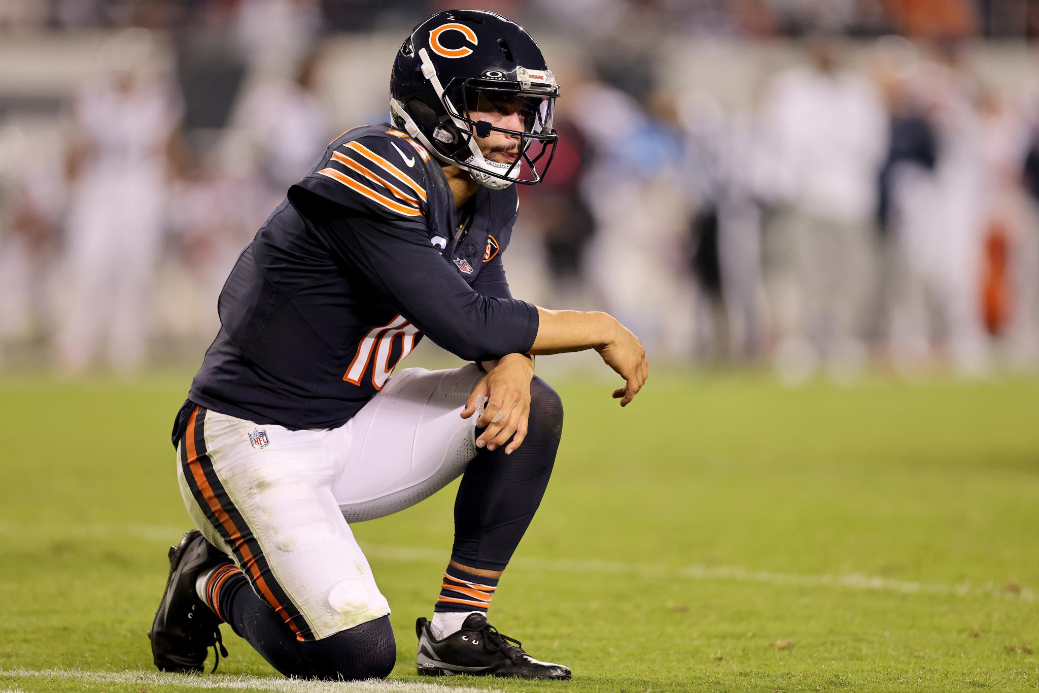 Caleb Williams of the Chicago Bears kneels on the field looking concerned during a game against the New England Patriots.