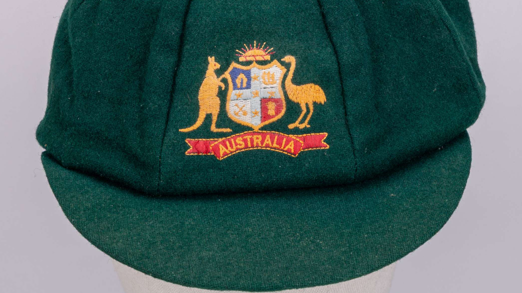 Picture of a dark green cap worn by Geoff Marsh. The Australian coat of arms is stitched to the front, while the cap is made from a felt green.