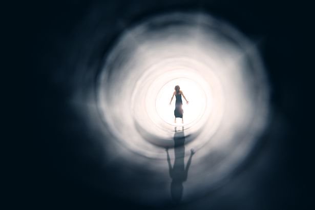 A conceptual image of the figure of a woman floating into the light at the end of a tunnel.