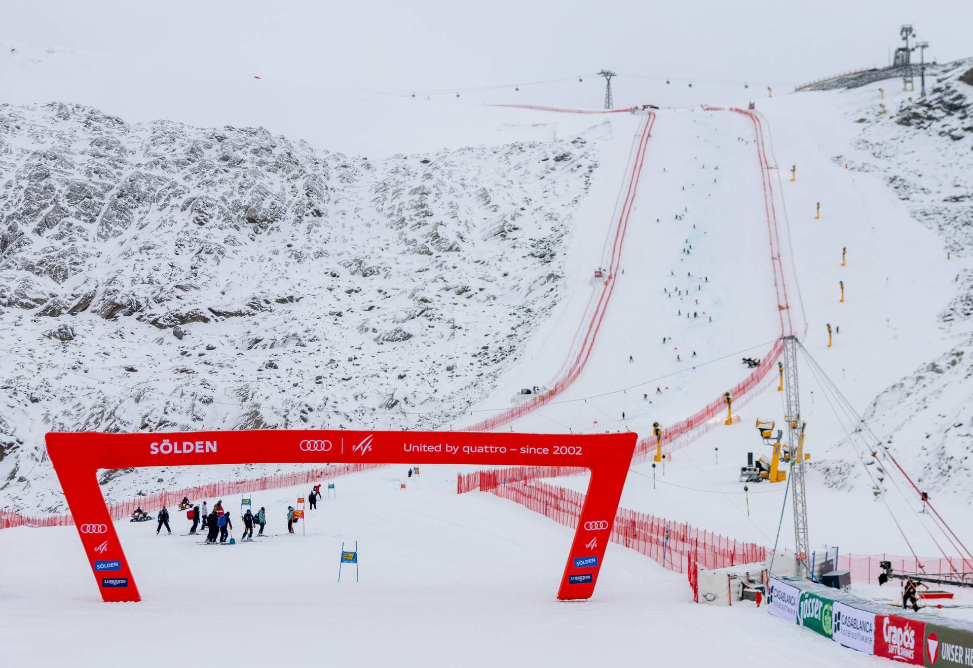Blick auf die schneebedeckte Skipiste in Sölden mit rotem Startbogen und Menschen am Pistenbeginn.