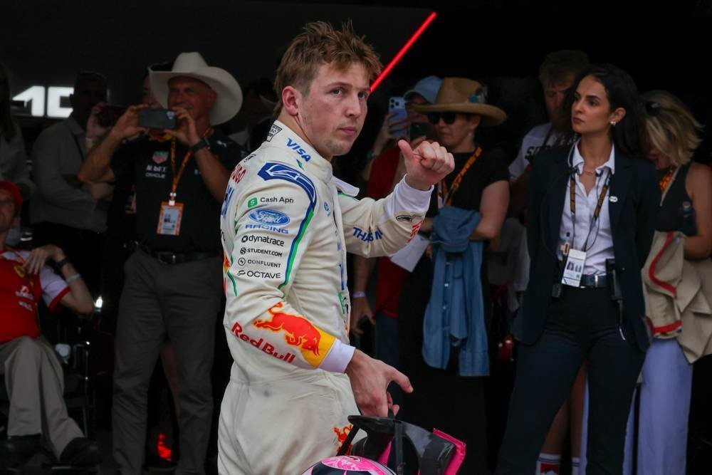 Racing driver in white Racing Bulls suit with Red Bull logo, holding a pink helmet in the paddock at the US Grand Prix in Austin, F1.