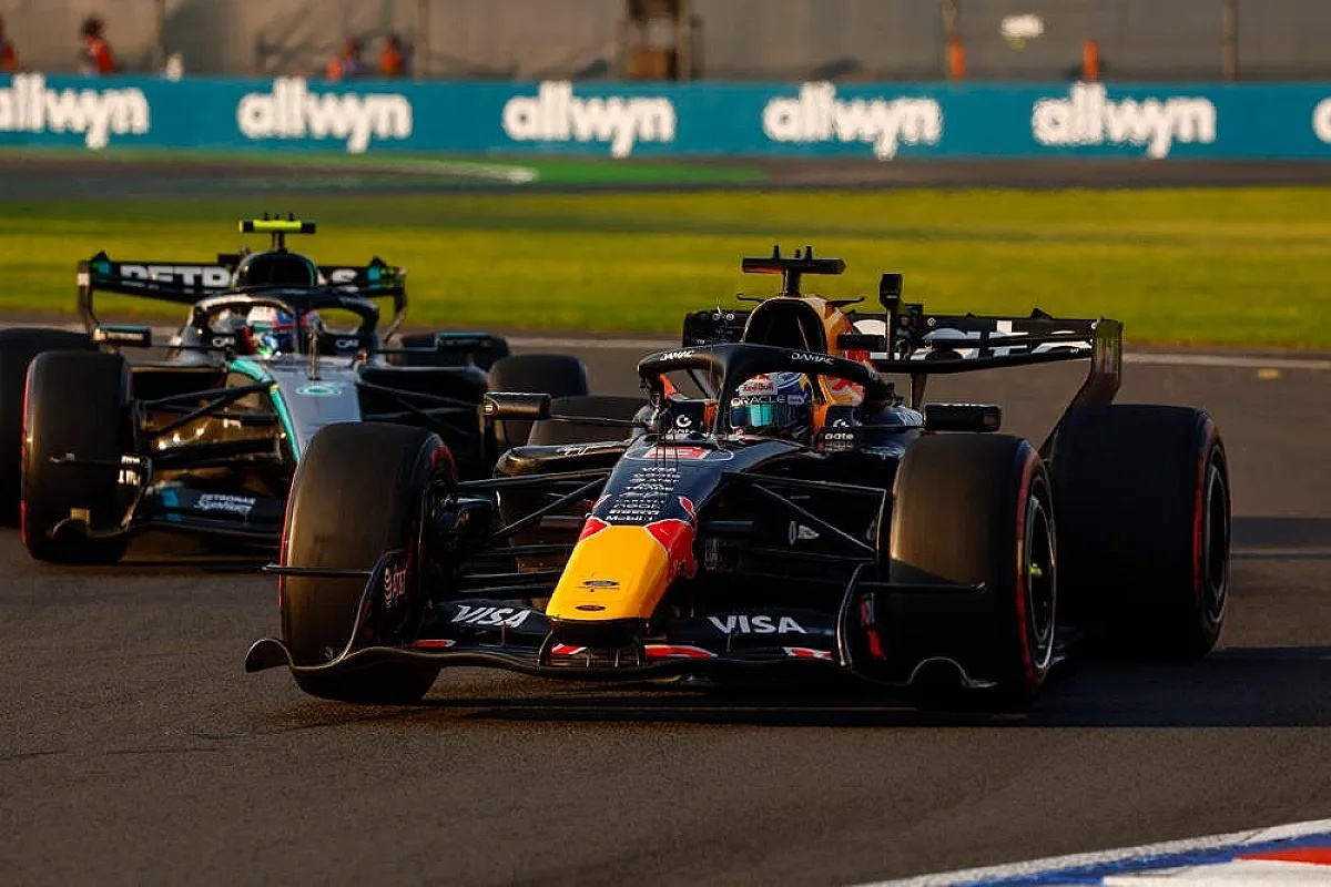 Red Bull RB22 F1 car with Visa livery on track, followed by a Mercedes car, at the Mexico Grand Prix, with Allwyn signage behind.