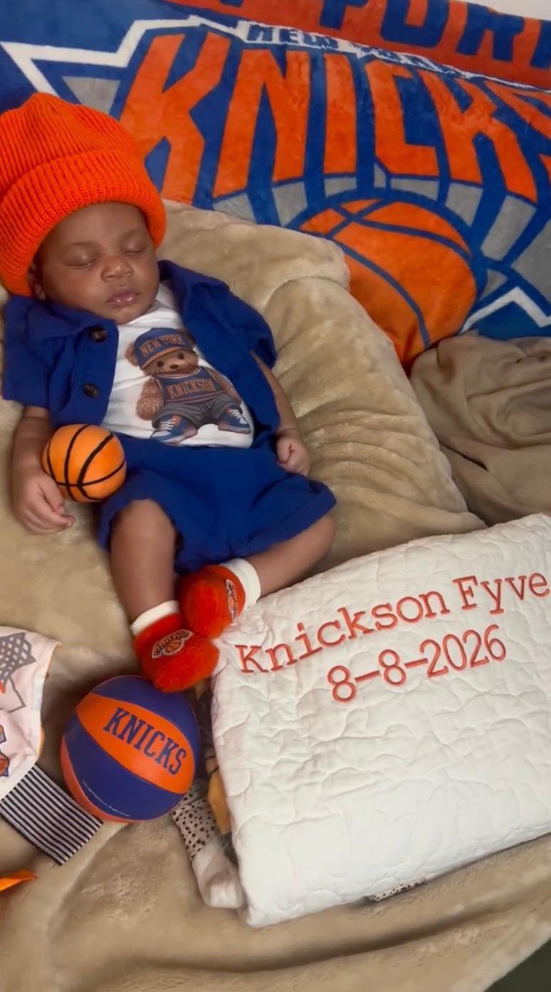 Newborn Knickson Fyve Bradford wearing Knicks-themed clothing and an orange beanie while sleeping next to basketballs and a personalized blanket.