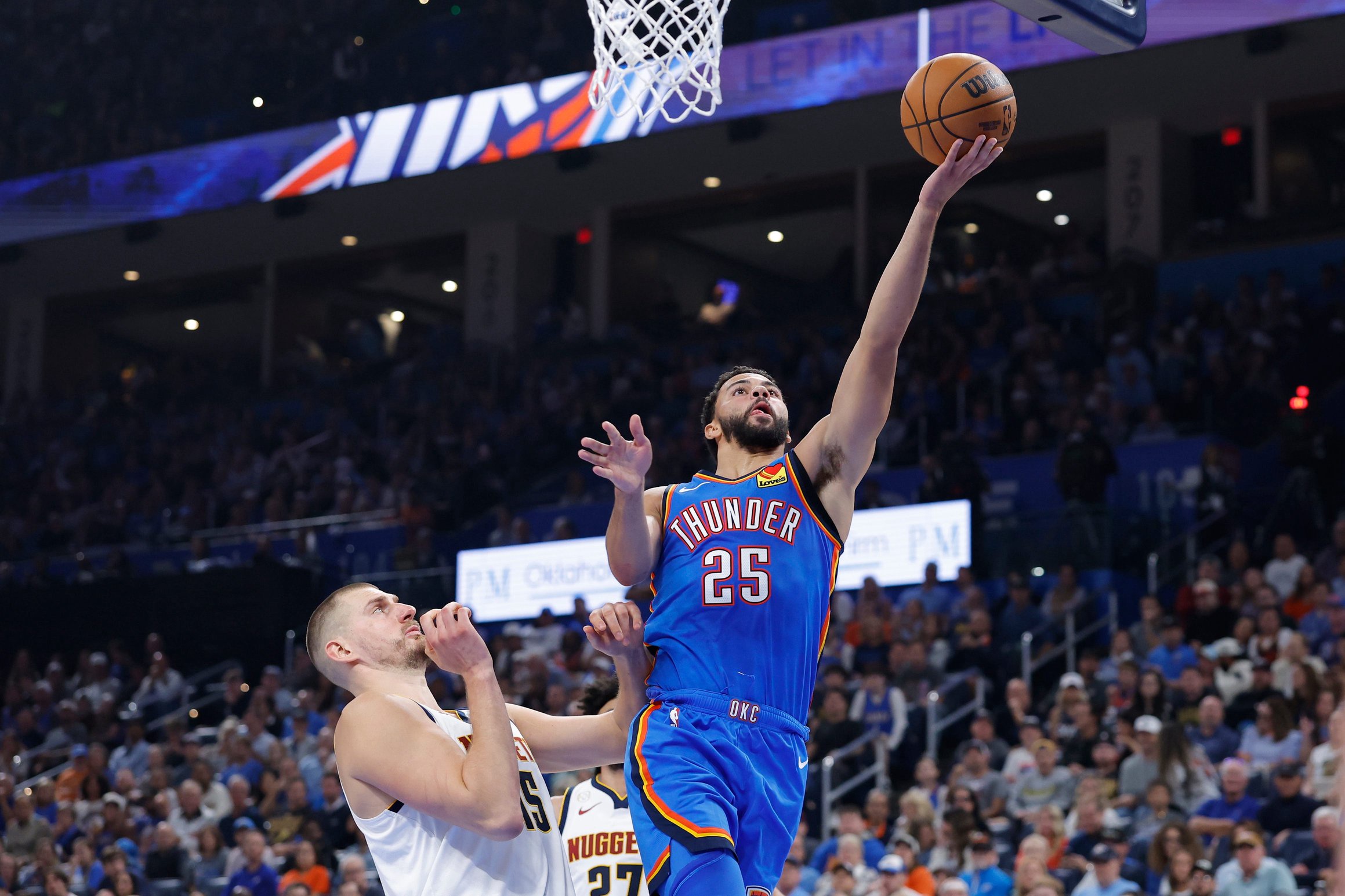 Oct 22, 2026; Oklahoma City, Oklahoma, USA; Oklahoma City Thunder guard Ajay Mitchell (25) goes up for a basket beside Denver Nuggets center Nikola Jokic (15) during the first half at Paycom Center. Mandatory Credit: Alonzo Adams-Imagn Images