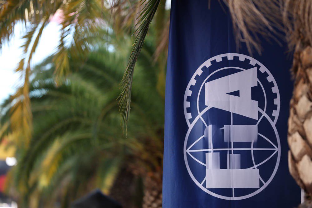 Blue FIA flag with white logo hanging among palm trees at a motorsport event, relevant to Formula 1 race regulations