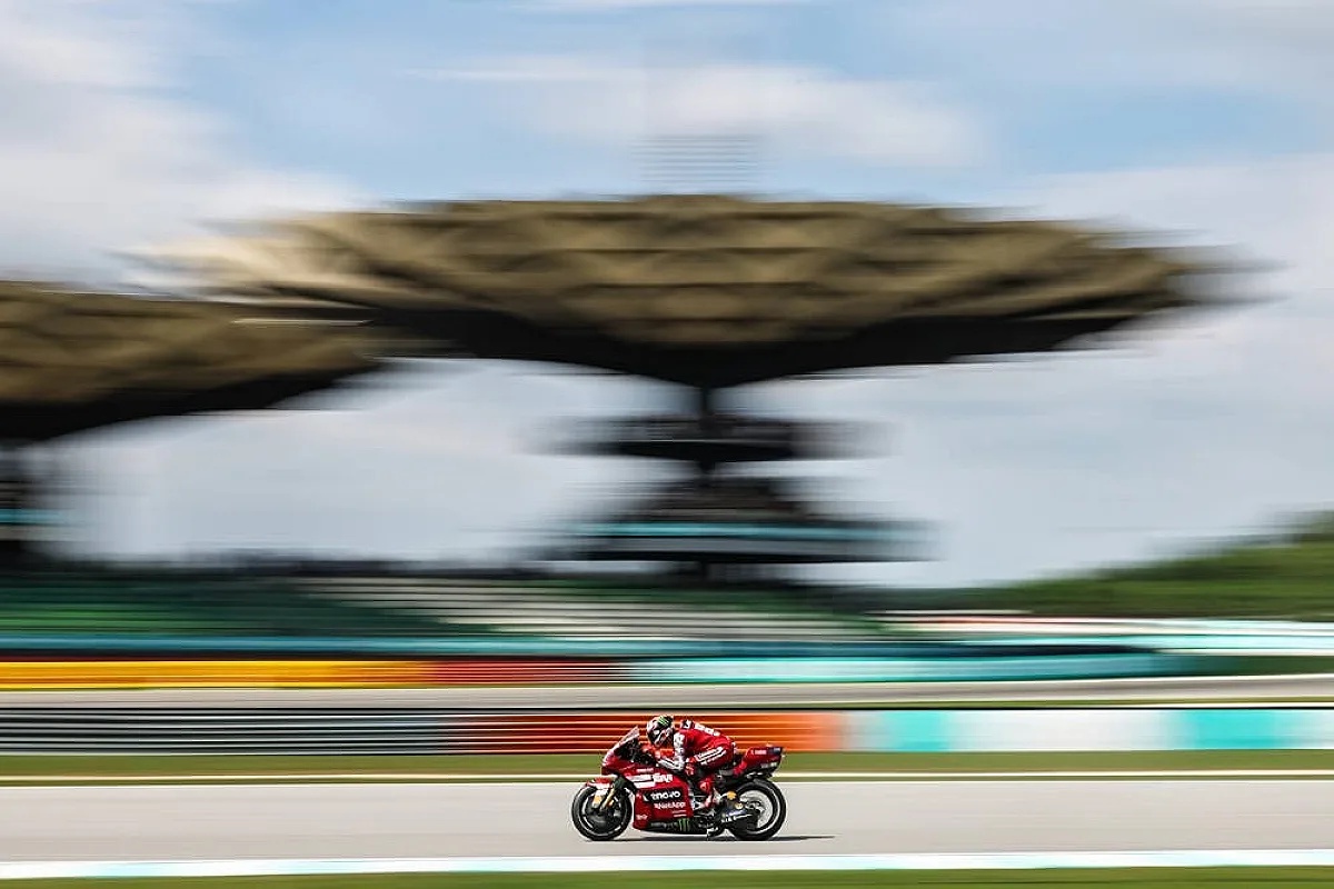 Francesco Bagnaia on his red Ducati MotoGP bike at Sepang, blurred grandstand canopy behind him