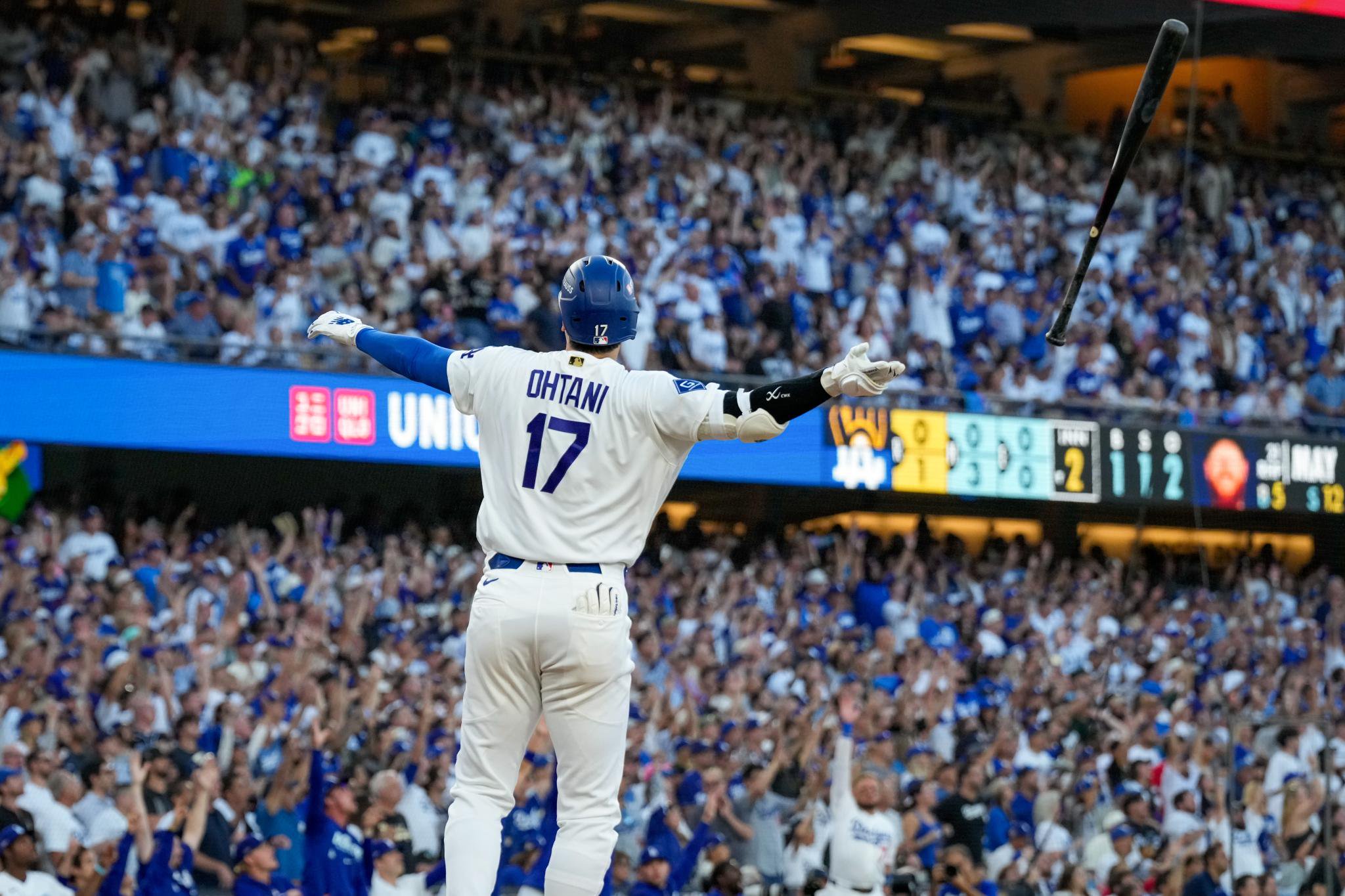 Los Angeles Dodgers designated hitter Shohei Ohtani celebrates a three-run home run with arms raised in front of a cheering crowd.