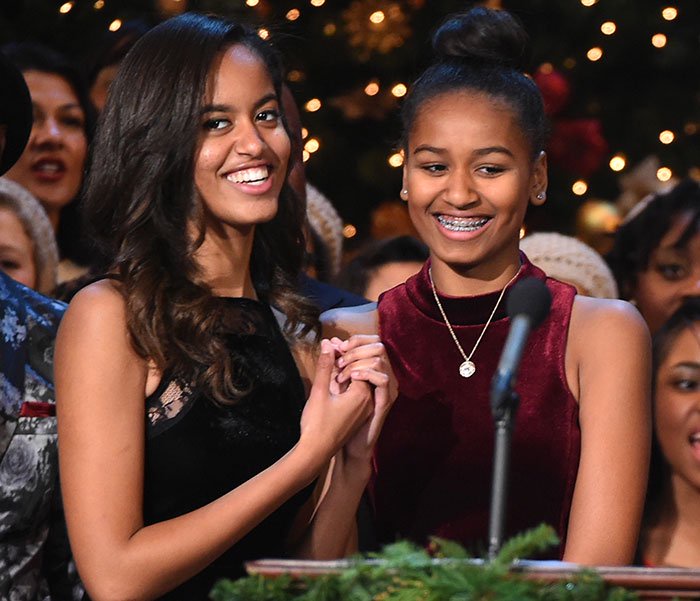 Sasha Obama and Malia smiling together at a festive party, Sasha showing off her figure beside her sister.
