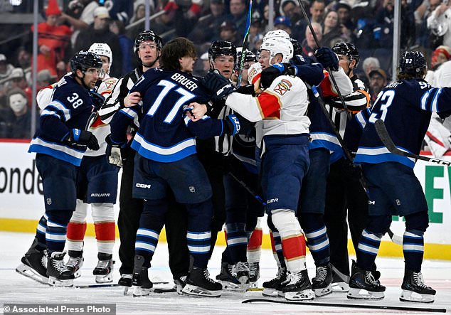 Winnipeg Jets' Tyrel Bauer (77) and Florida Panthers' Brady Tkachuk (8) grab each other during second period NHL action in Winnipeg on Tuesday, Oct. 27, 2026. (Fred Greenslade/The Canadian Press via AP)