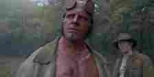 Hellboy looks up while standing at the edge of a wood in Hellboy: The Crooked Man