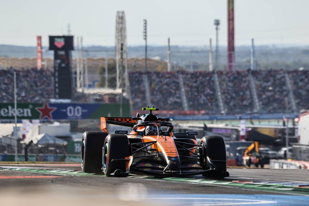 Lando Norris in a McLaren Formula 1 car, papaya livery, taking a corner at the US Grand Prix in Austin with grandstands behind