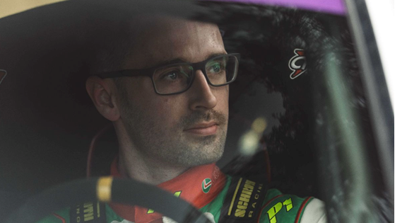 Meirion Evans sitting in the car in his race suit, wearing glasses.