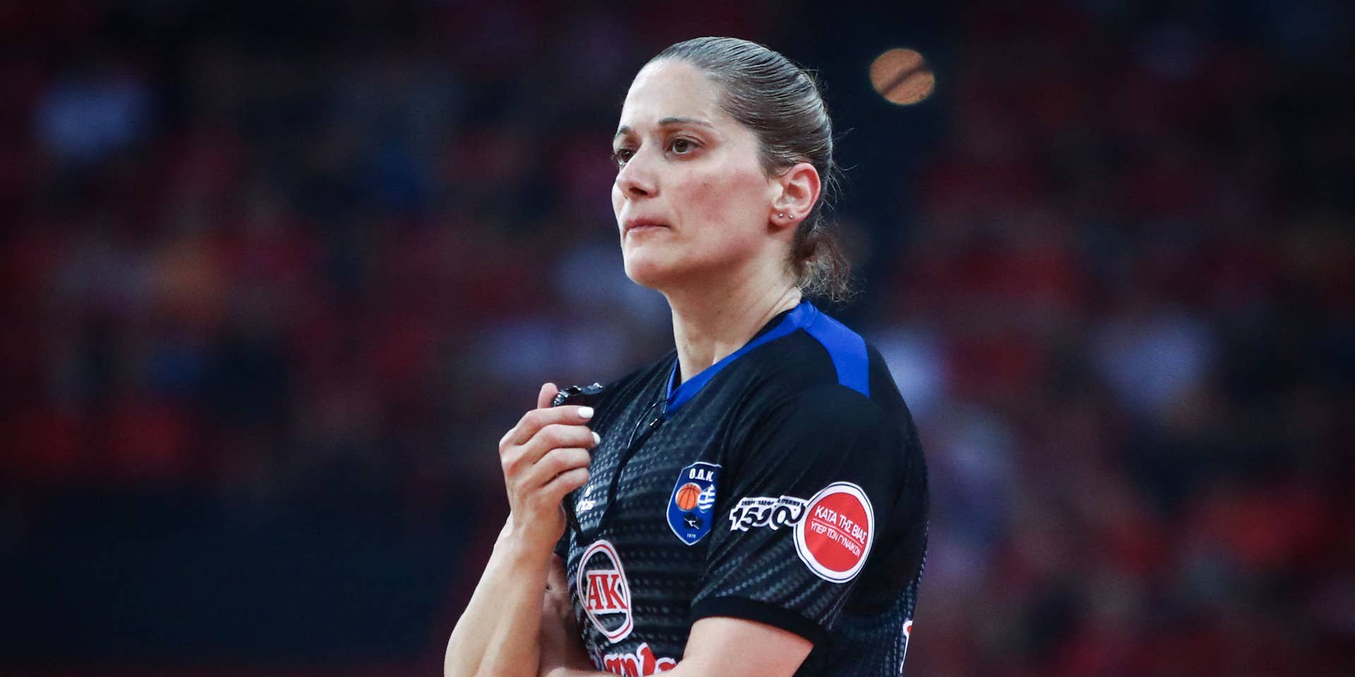 Die Schiedsrichterin Vasiliki Tsaroucha steht in ihrem dunkelgrau-blauen Trikot auf dem Basketballfeld und blickt mit ernster Miene zur Seite.