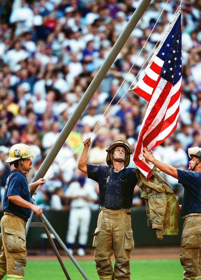 Firefighters hoist an American flag before the start of Game 1 of the 2001 World Series.