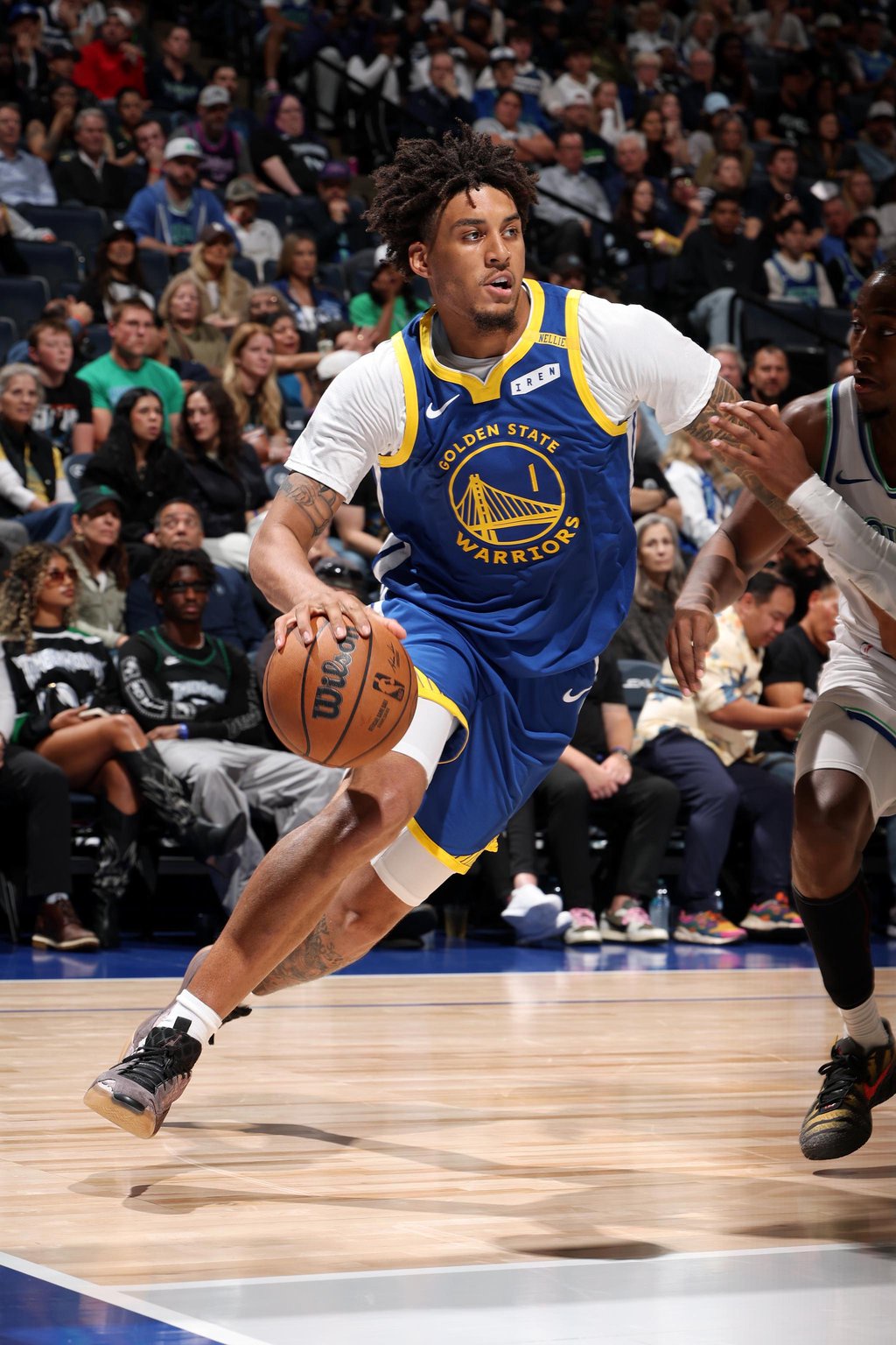 A Golden State Warriors player dribbles the basketball past a Minnesota Timberwolves defender during a game.