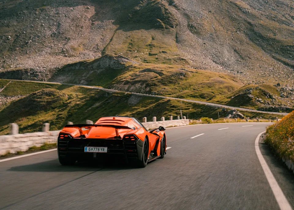 A bright orange sports car navigating a winding road in a mountainous landscape.