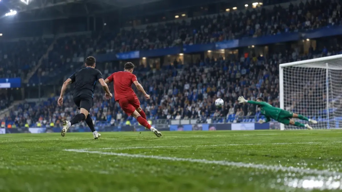 Late-match football action at RCDE Stadium as a shot heads toward goal