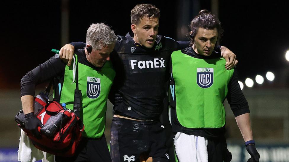 Kieran Hardy helped off the pitch by Ospreys medics