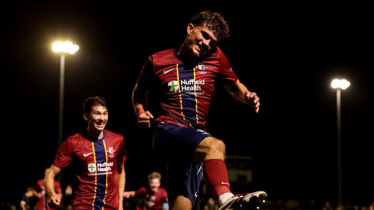 Cardiff Met's Mitchell Ford in a red with blue vertical stripe jumps in the air to celebrate scoring
